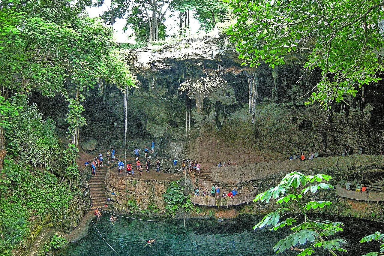 Cenote Zací in Valladolid: Besucher auf Treppen und Terrassen unter einem überhängenden Kalksteingewölbe über grünem Wasser