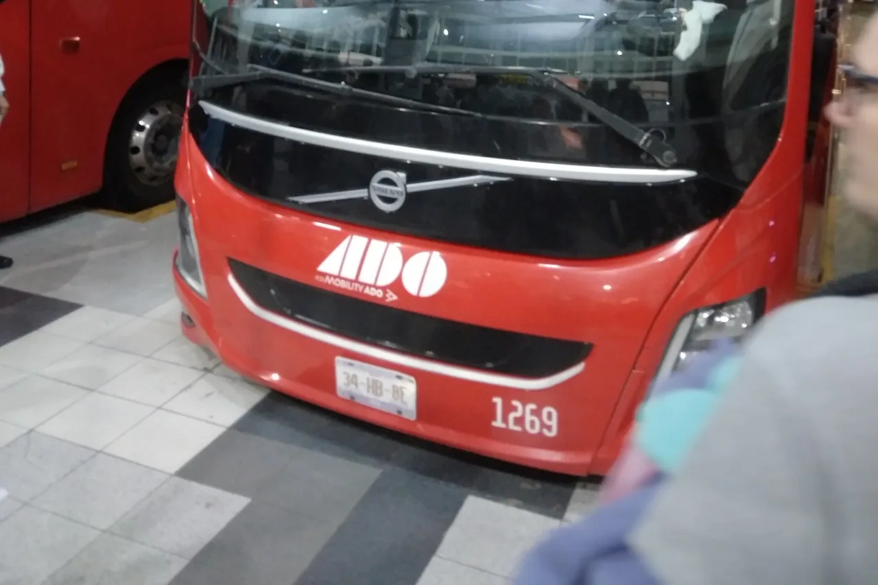 Frontansicht eines roten ADO-Reisebusses mit Logo im Busterminal