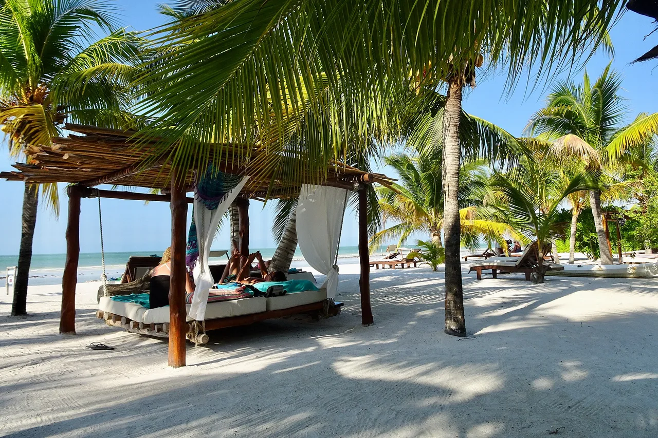 A Holbox beach lined with palm trees, daybeds and thatched shelters at the water's edge