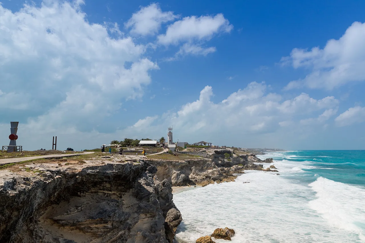 The rocky point of Punta Sur on Isla Mujeres, low cliffs struck by waves with a lighthouse beyond