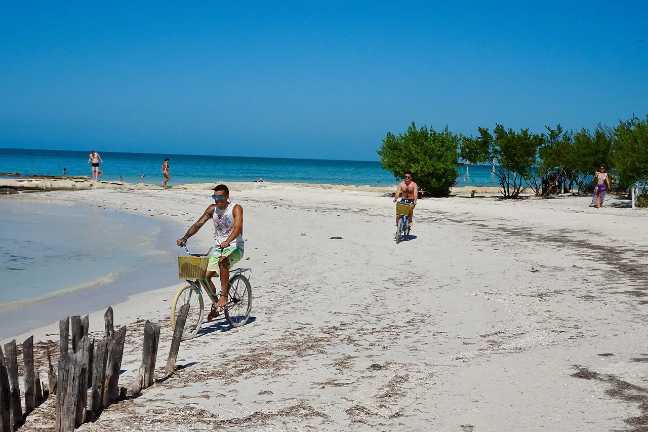 Ein Radfahrer fährt über den weißen Sand des Strandes von Holbox vor ruhigem, flachem Wasser