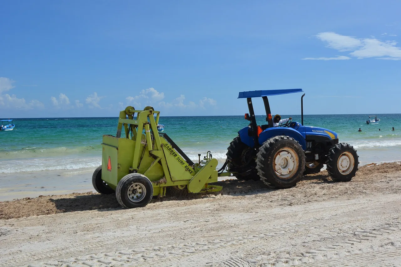 Ein Traktor zur Strandreinigung auf dem Sand vor dem türkisfarbenen Meer in Tulum, Mexiko