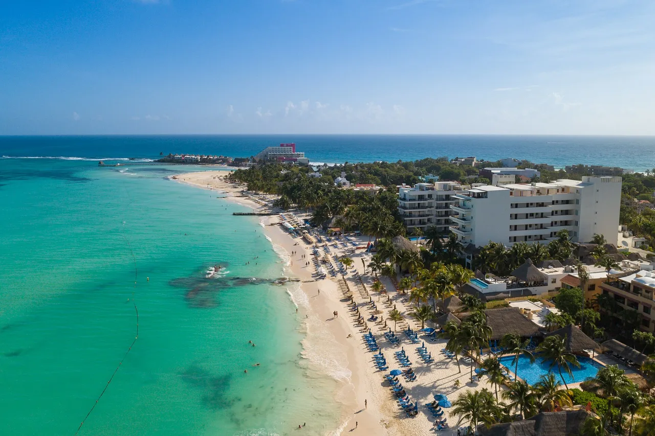 Aerial view of Playa Norte on Isla Mujeres: white sand, shallow turquoise water, palms and hotels on the shore.