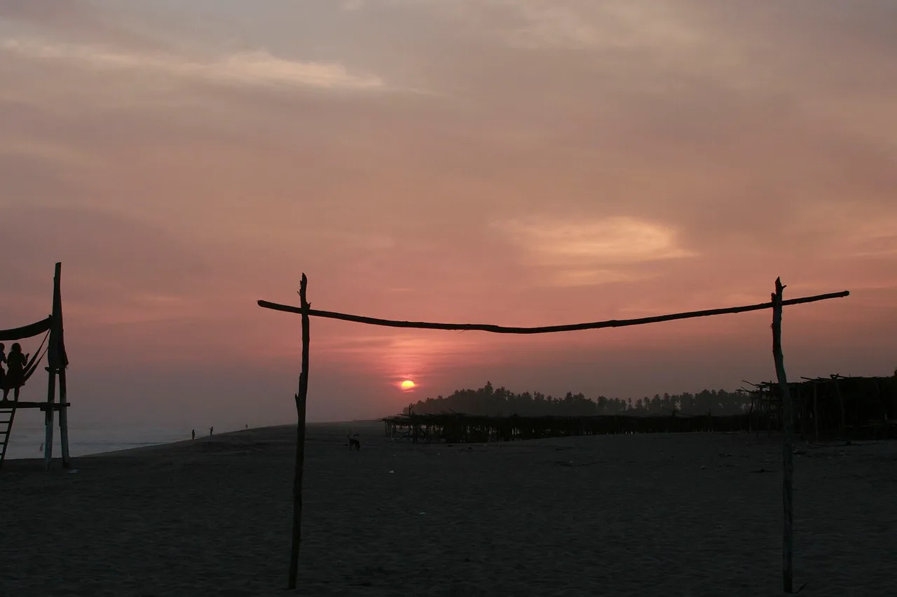 Atardecer en una playa de Tulum, dos postes de madera recortados contra el cielo rosado