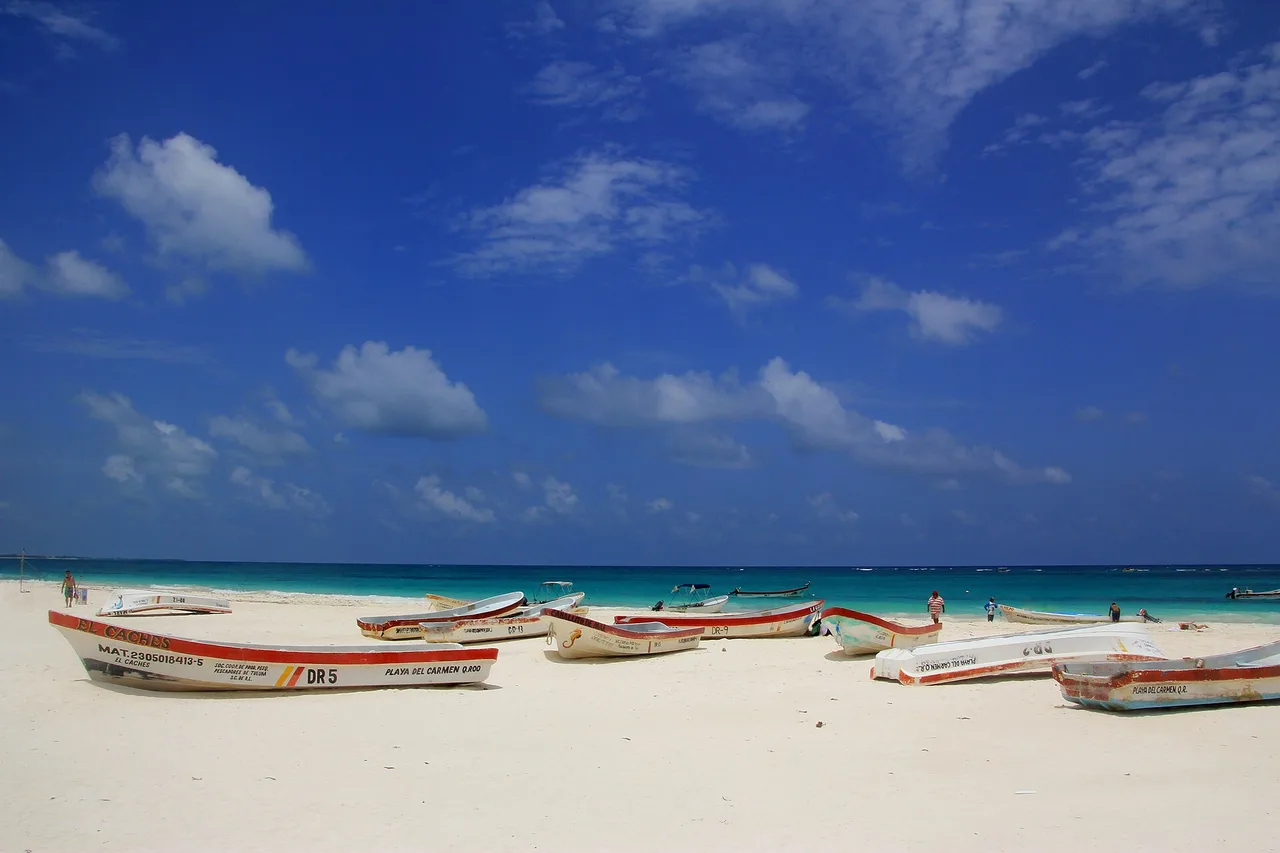 Barcas de pesca sobre la arena blanca de una playa de Tulum, con agua turquesa y cielo despejado