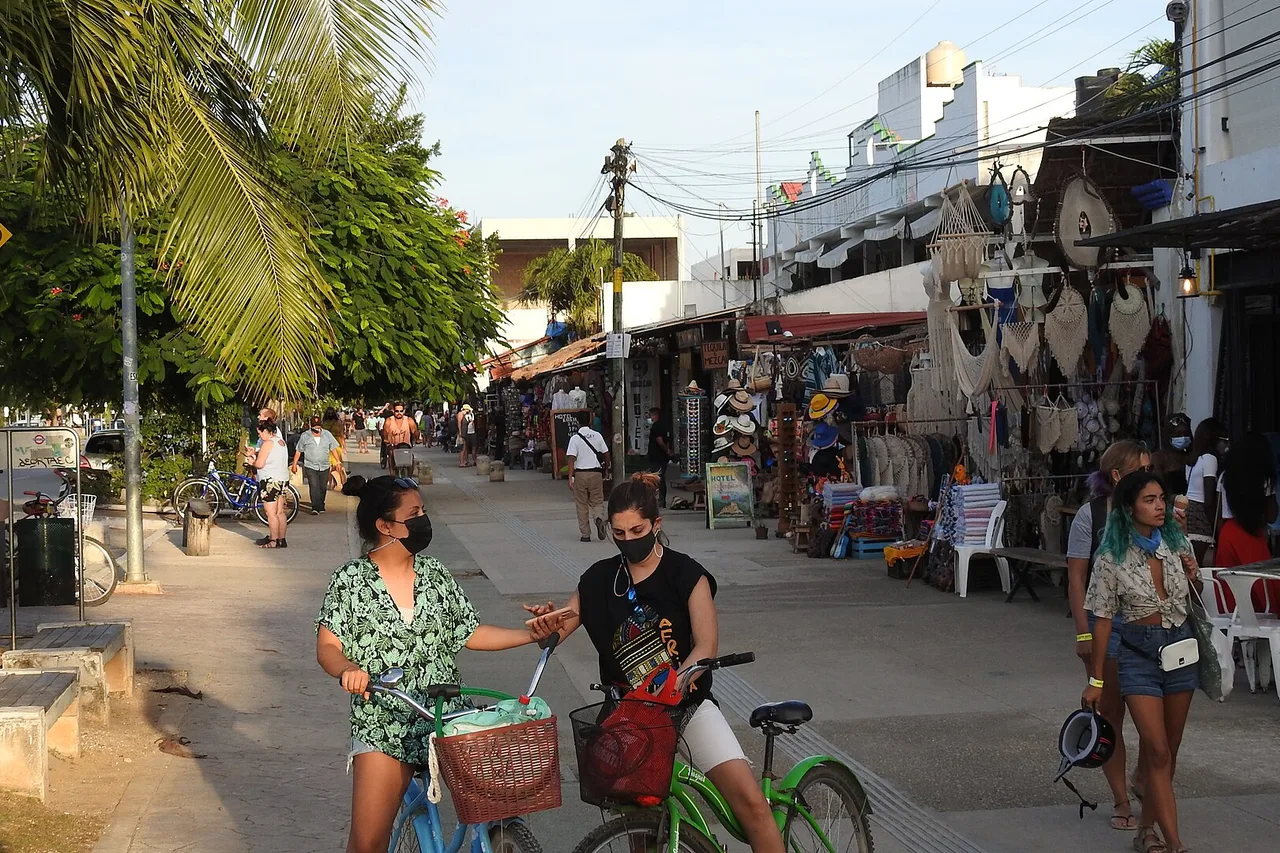 Una calle comercial del centro de Tulum, con tiendas, terrazas y gente en bicicleta