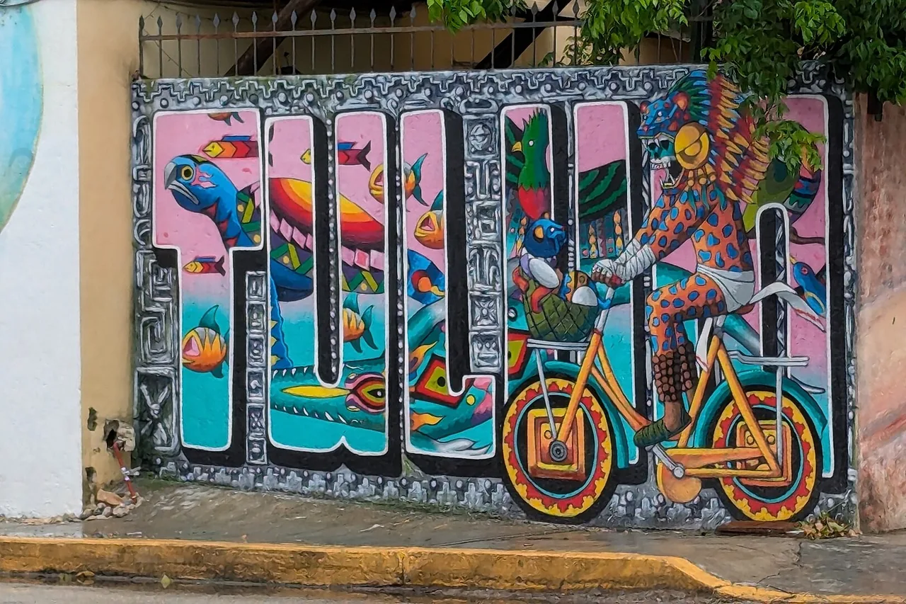 Un mural colorido con las letras de Tulum y un personaje en bicicleta, en una pared del centro
