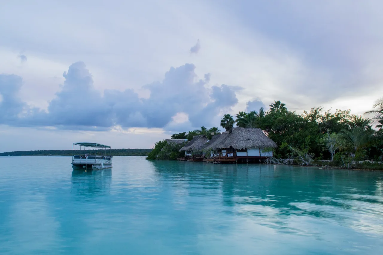 Le acque turchesi e verde chiaro della laguna di Bacalar, una barca ormeggiata davanti alla riva boscosa