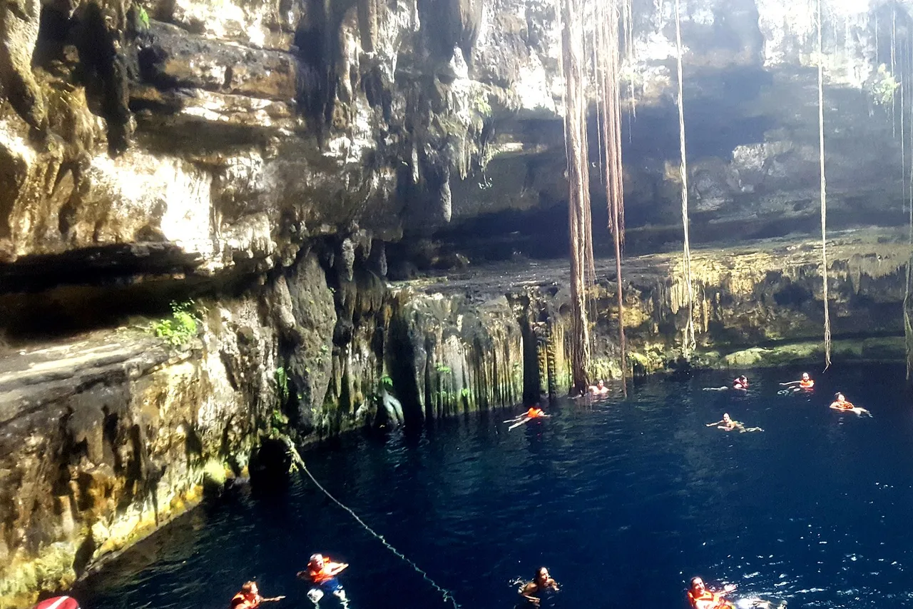 Bagnanti in un cenote in grotta dello Yucatán, radici e stalattiti che scendono dalla volta