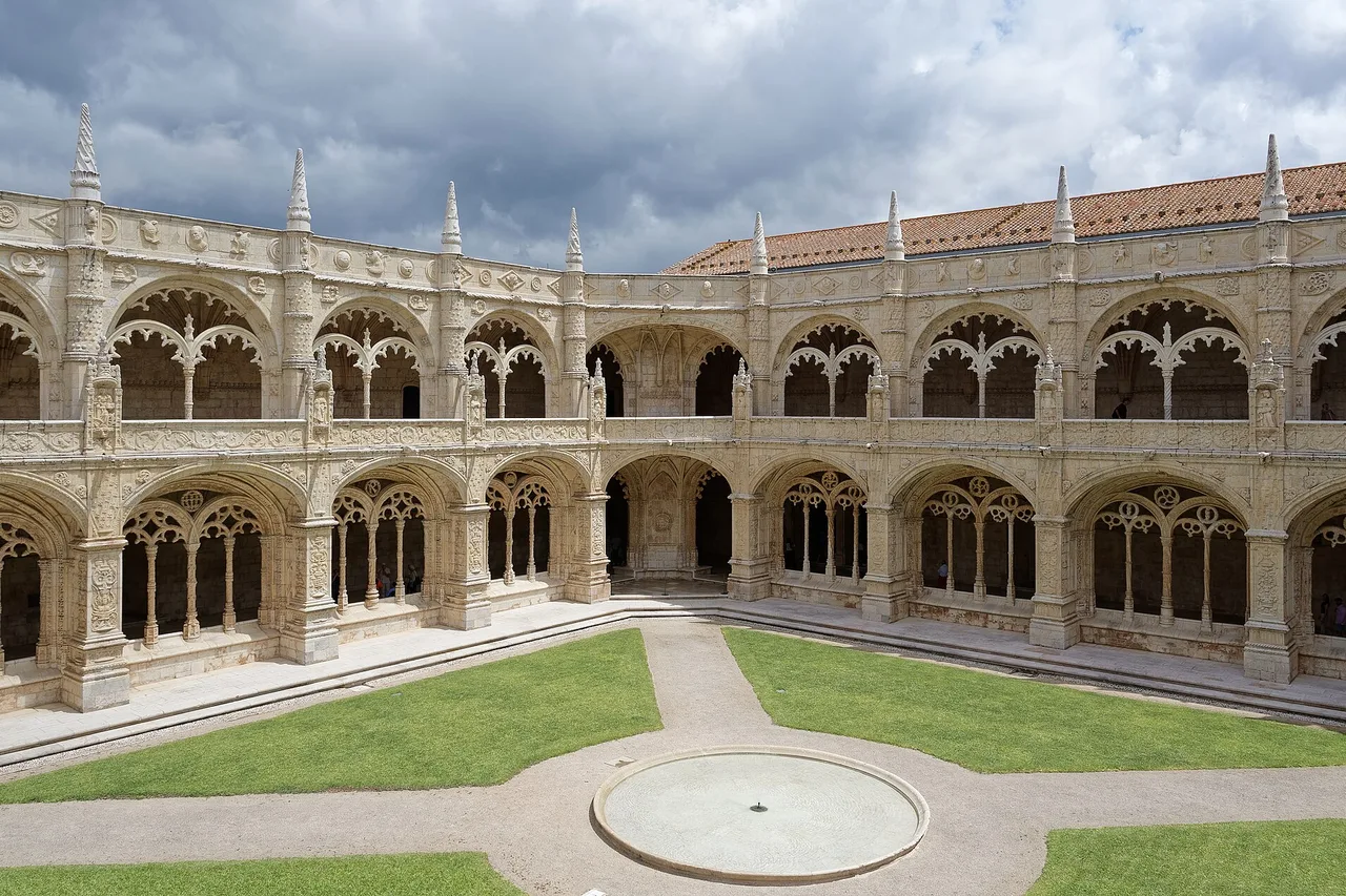The two-storey cloister of the Jerónimos Monastery in Belém, with finely carved arches of pale limestone around a lawn courtyard