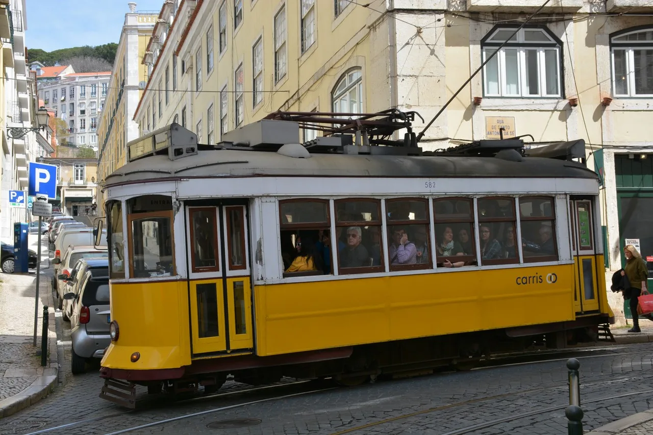 A yellow Carris tram in a narrow cobbled street in Lisbon’s Alfama district, between tall buildings with pale facades
