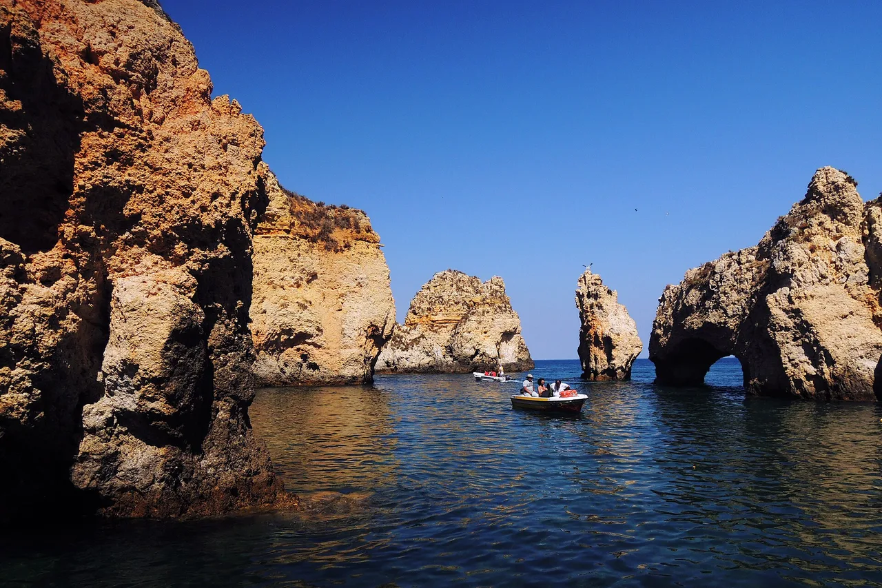 Felsformationen und Felsentor der Ponta da Piedade bei Lagos mit einem Ausflugsboot im blauen Wasser