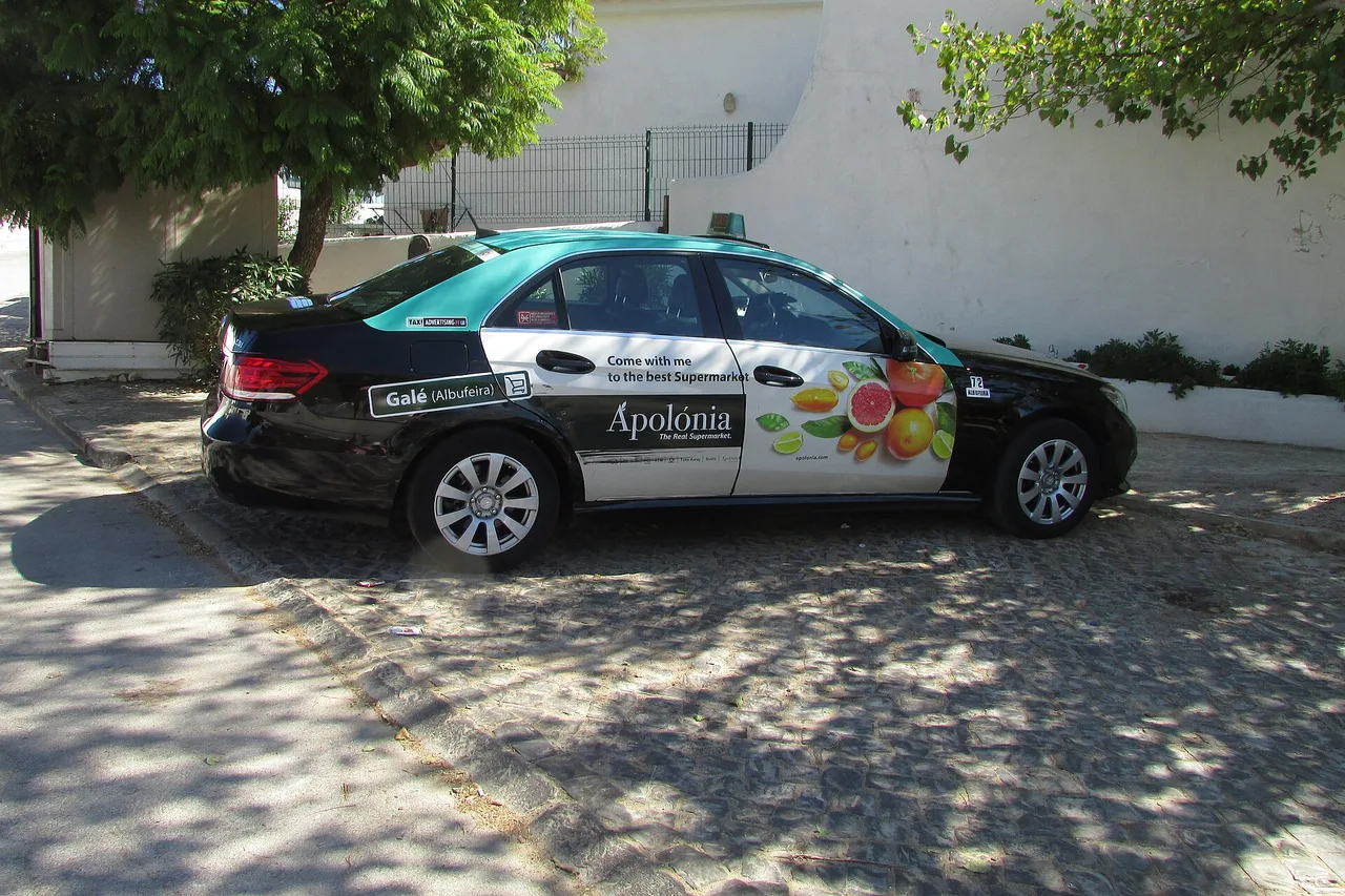 Schwarz-grünes Taxi mit Werbung auf den Türen, geparkt auf Kopfsteinpflaster in Albufeira
