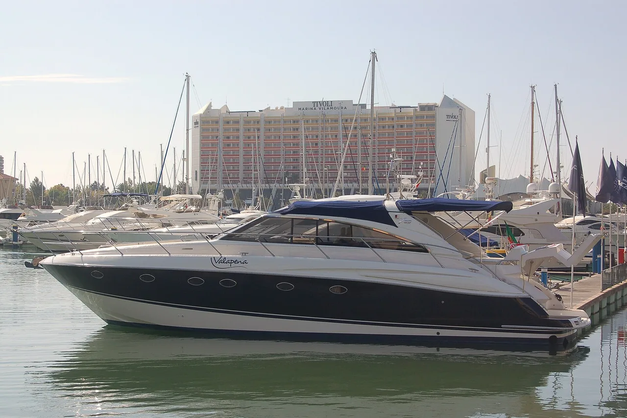 Motoryacht im Hafen der Marina von Vilamoura, dahinter ein Hotelhochhaus und Segelmasten