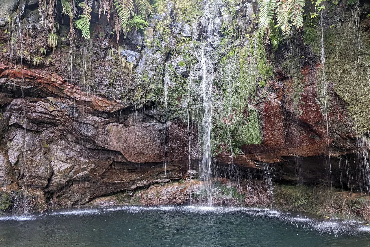 Cascate che scendono su rocce rosse e coperte di muschio nel piccolo lago delle 25 Fontes, a Madeira