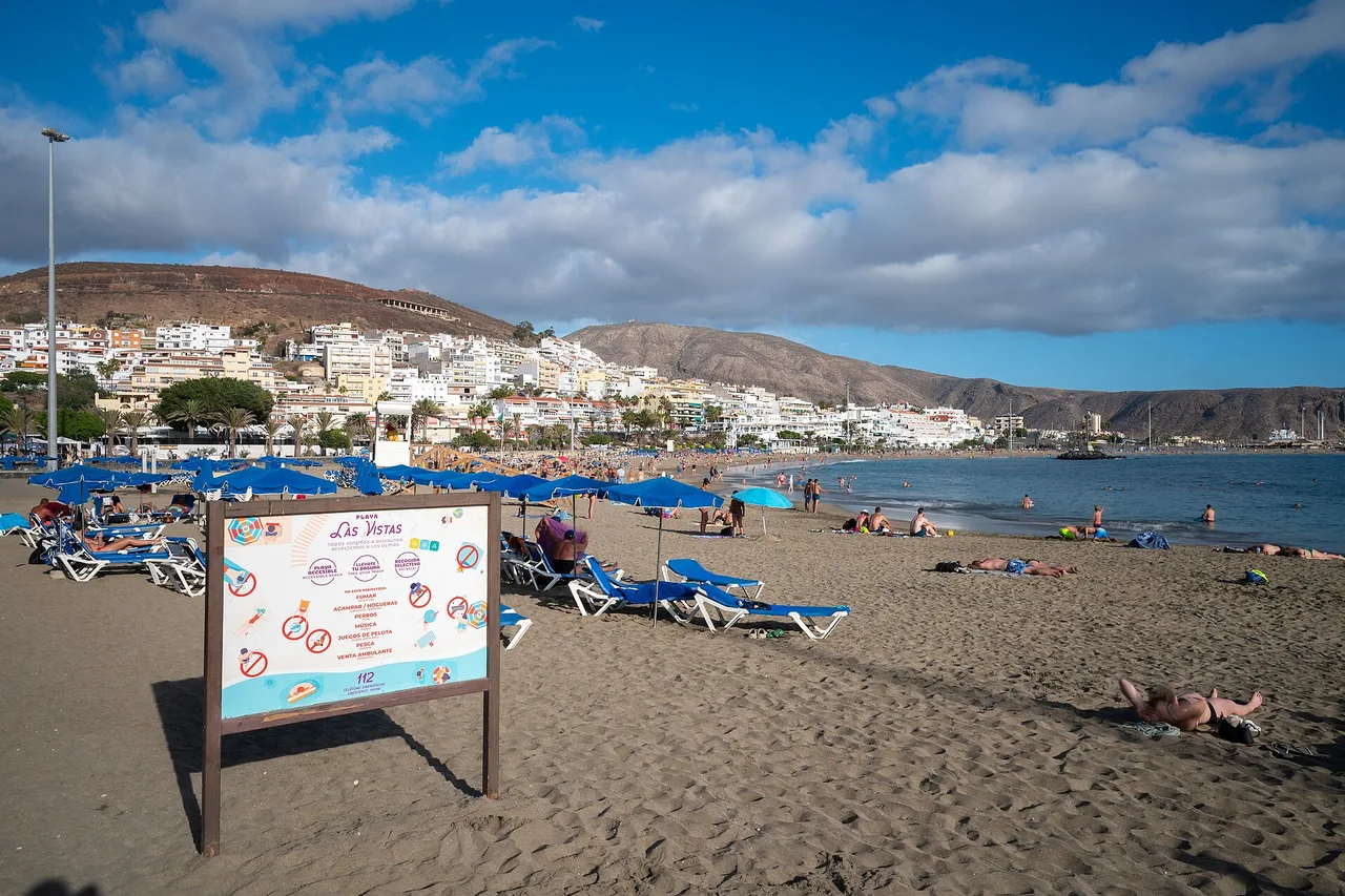 Der Strand Las Vistas mit seinen blauen Sonnenschirmen vor den Häusern von Los Cristianos im Süden Teneriffas