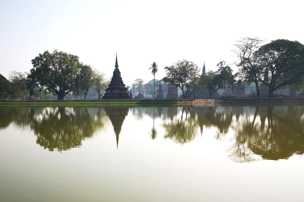 Ein Chedi im Geschichtspark Sukhothai spiegelt sich am frühen Morgen in einem Wasserbecken, Thailand