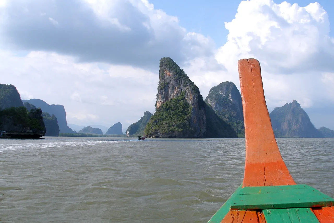 Proa de una barca longtail frente a los farallones calizos de la bahía de Phang Nga bajo un cielo cubierto