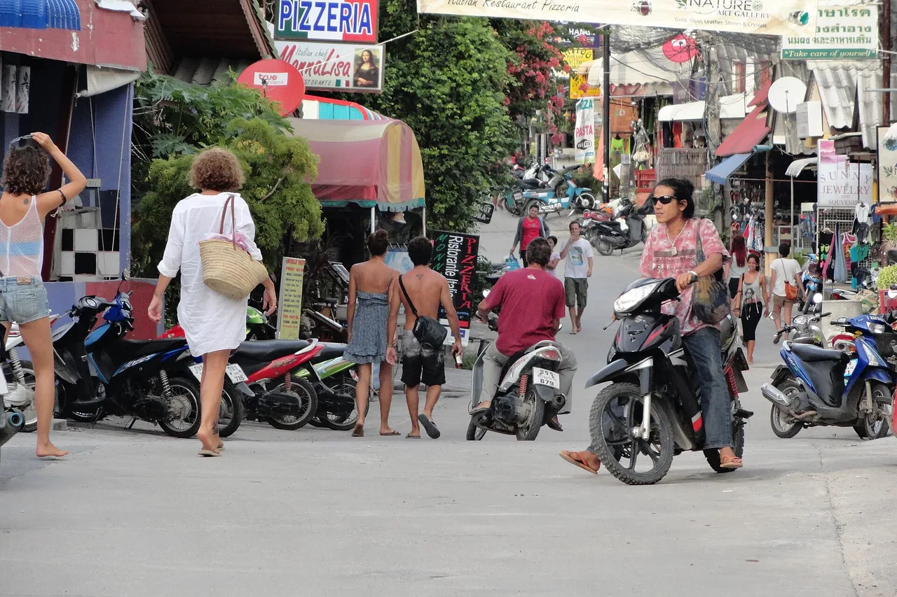 Einkaufsstraße in Haad Rin mit geparkten Rollern und Geschäften, Koh Phangan, Thailand