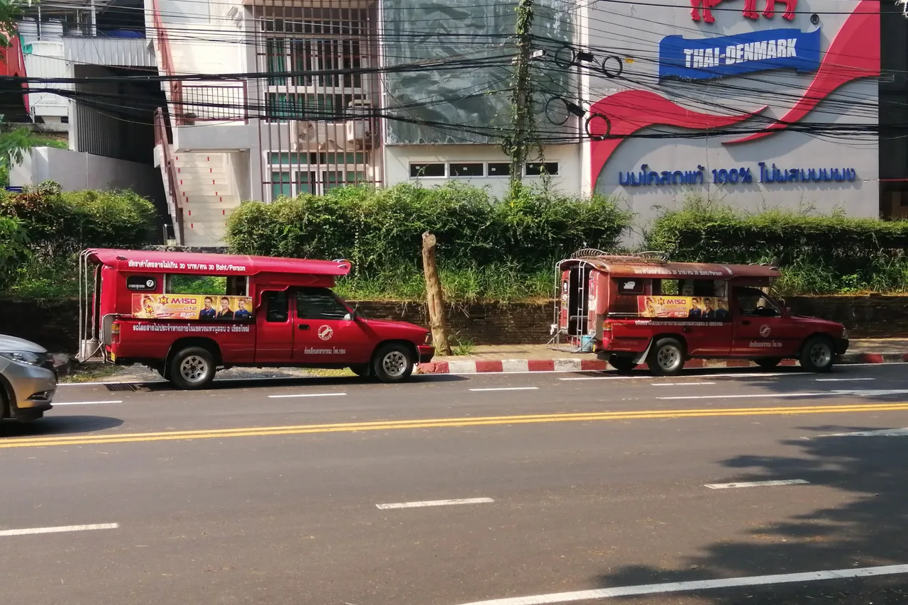A line of red songthaews, the shared taxis of Chiang Mai, parked along a street