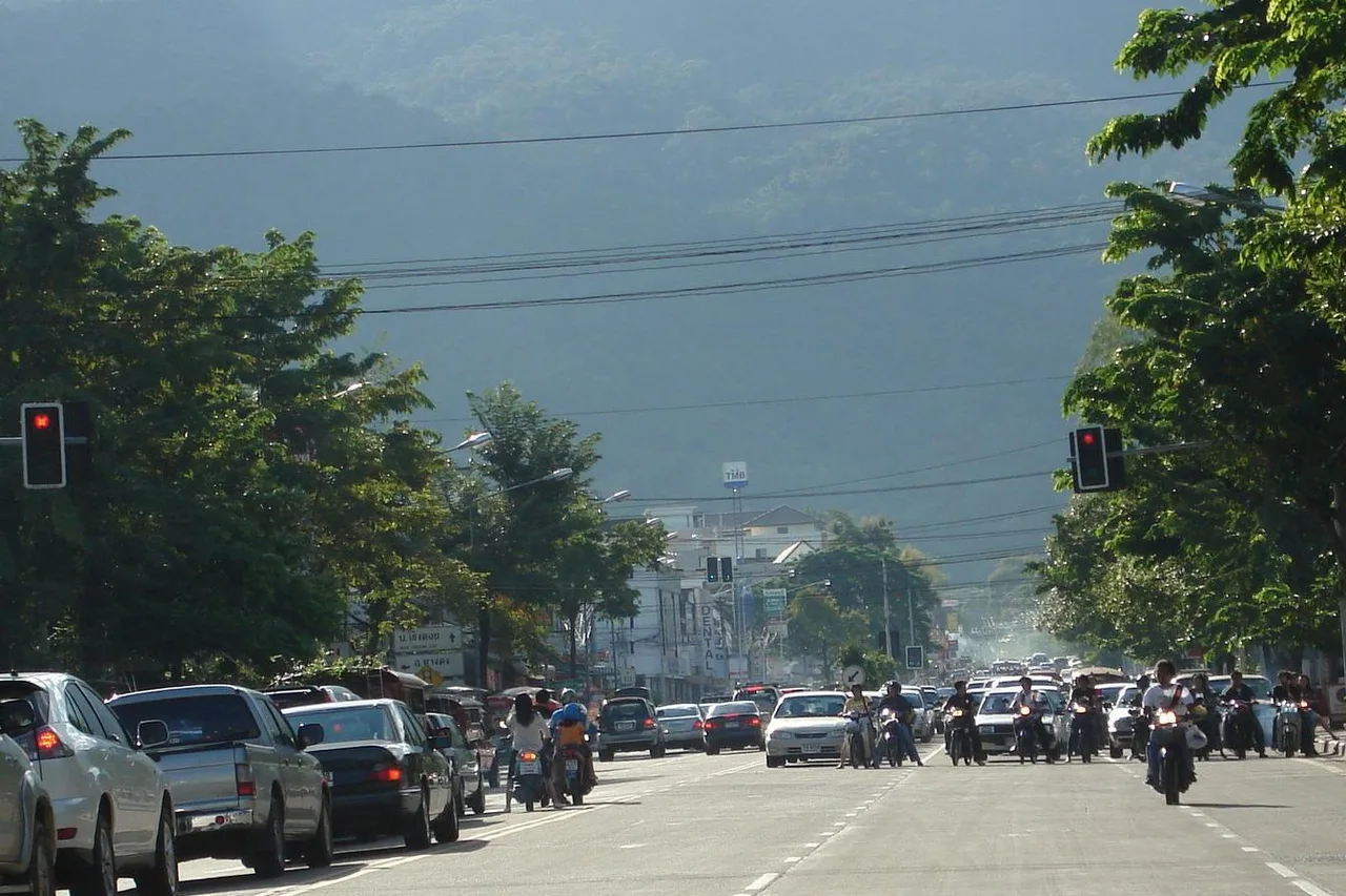 Autos und Roller an einer Ampel auf der Suthep Road in Chiang Mai, dahinter ein bewaldeter Berg