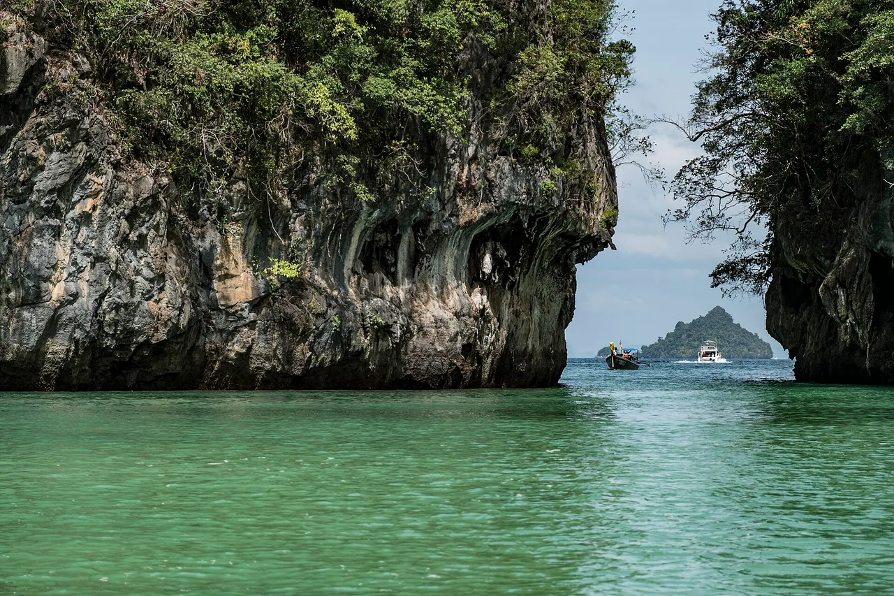 Le lagon de Hong Island à l’eau émeraude, avec à gauche une paroi rocheuse en surplomb creusée par l’érosion et, au fond, un bateau d’excursion