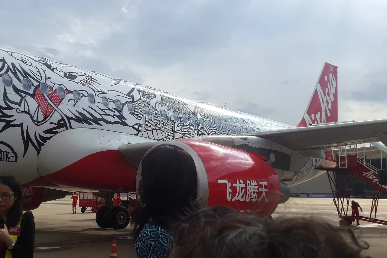 An AirAsia aircraft in a black-and-white special livery on the apron at Don Mueang, with waiting passengers in the foreground