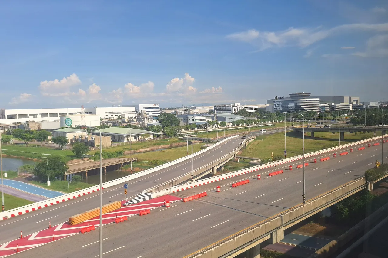 View from the Airport Rail Link as it nears Suvarnabhumi: elevated roads and airport-zone buildings under a blue sky