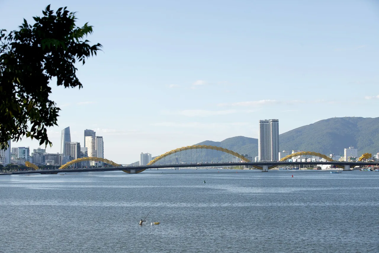 Le pont du Dragon de Da Nang au-dessus du fleuve Han, avec les immeubles de la ville et des montagnes au fond