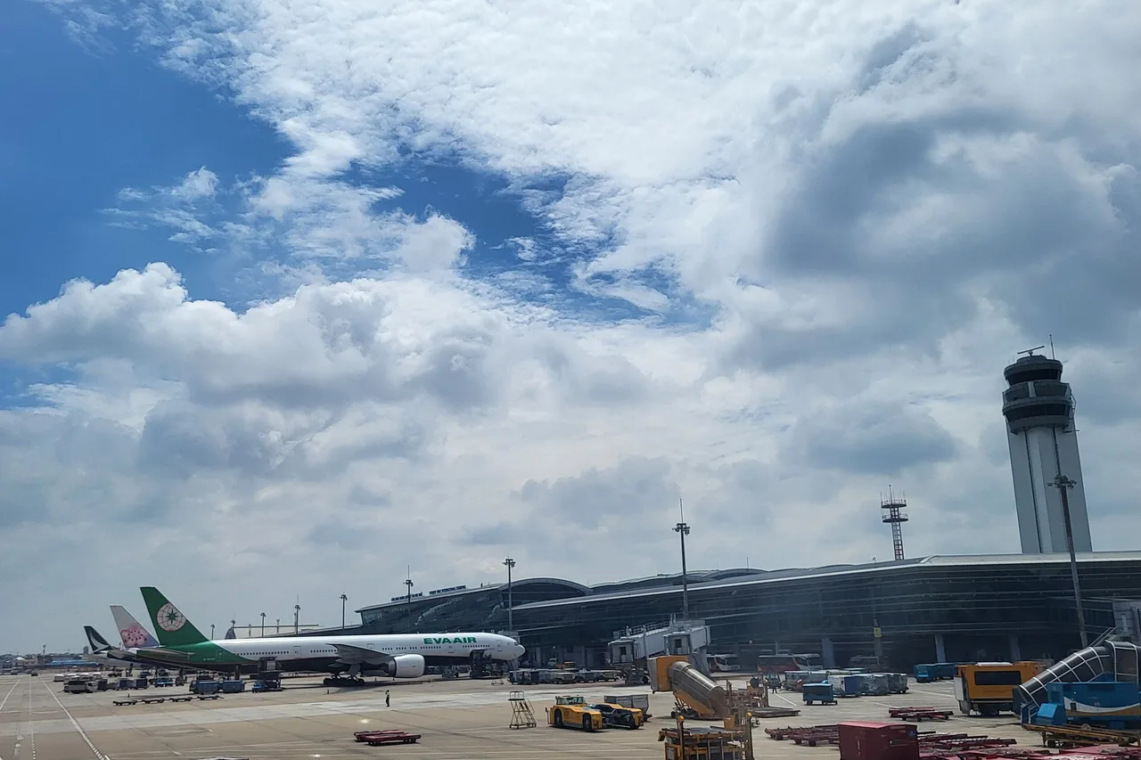 Kontrollturm und internationales Terminal des Flughafens Tân Sơn Nhất vom Vorfeld aus, davor abgestellte Flugzeuge unter bewölktem Himmel