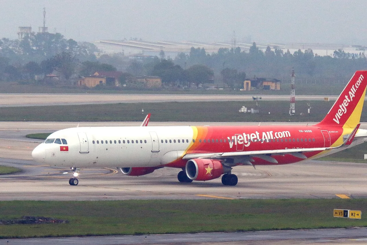 Ein rot-weißer Airbus A321 von VietJet Air rollt über das Flughafengelände von Hanoi, im Hintergrund Dunst und Bäume
