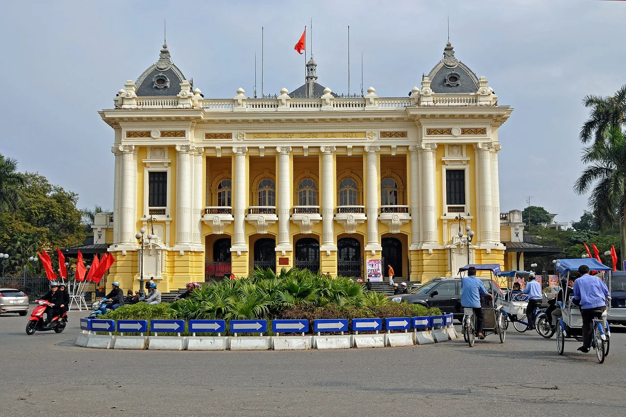 L'opéra de Hanoï, jaune et blanc, de style colonial avec colonnes et dômes, devant un rond-point fleuri