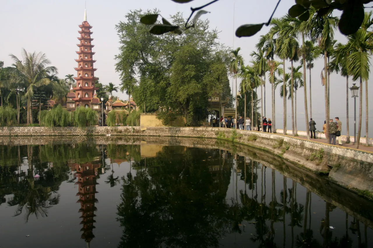 La pagode rouge Trấn Quốc se reflète dans un bassin au bord du lac de l'Ouest, entourée de palmiers et d'arbres
