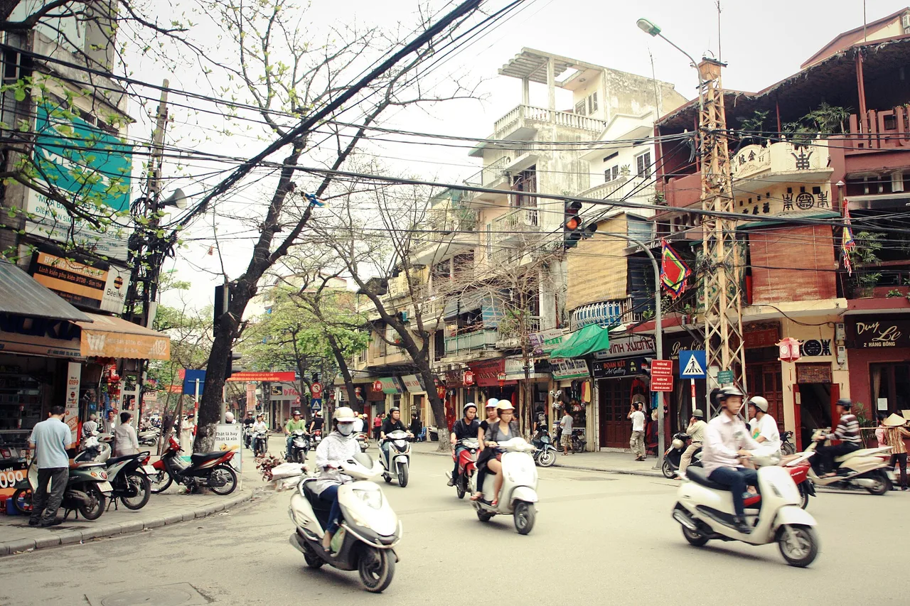Rue animée du vieux quartier de Hanoï avec des scooters, des fils électriques, des enseignes et des maisons étroites