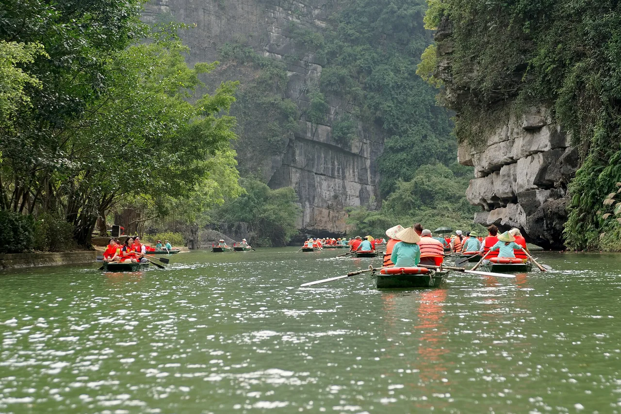 Barche a remi con visitatori su un fiume tra ripide pareti carsiche a Trang An, vicino a Ninh Binh.
