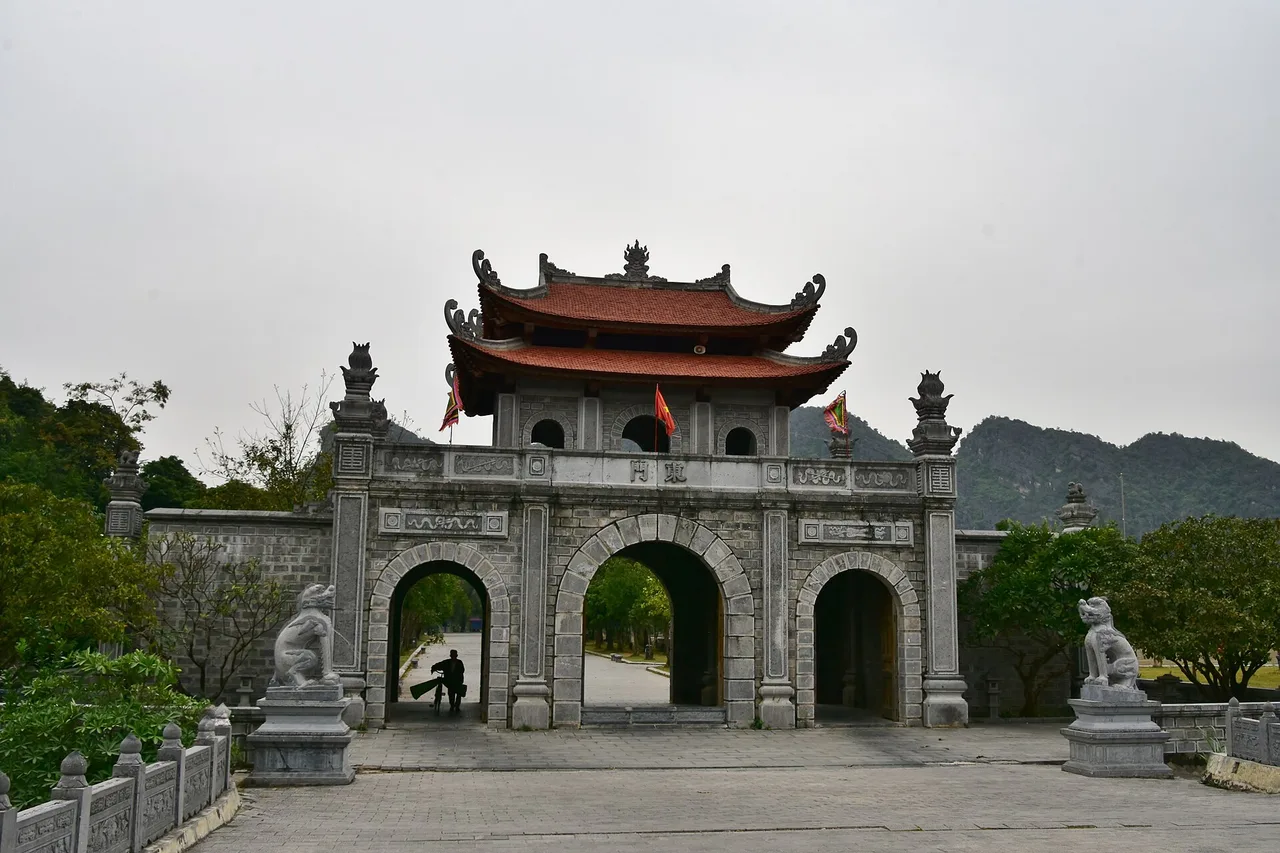 The gate with its curved tiled roof at the temple of the ancient capital Hoa Lu, with stone lions and limestone hills behind
