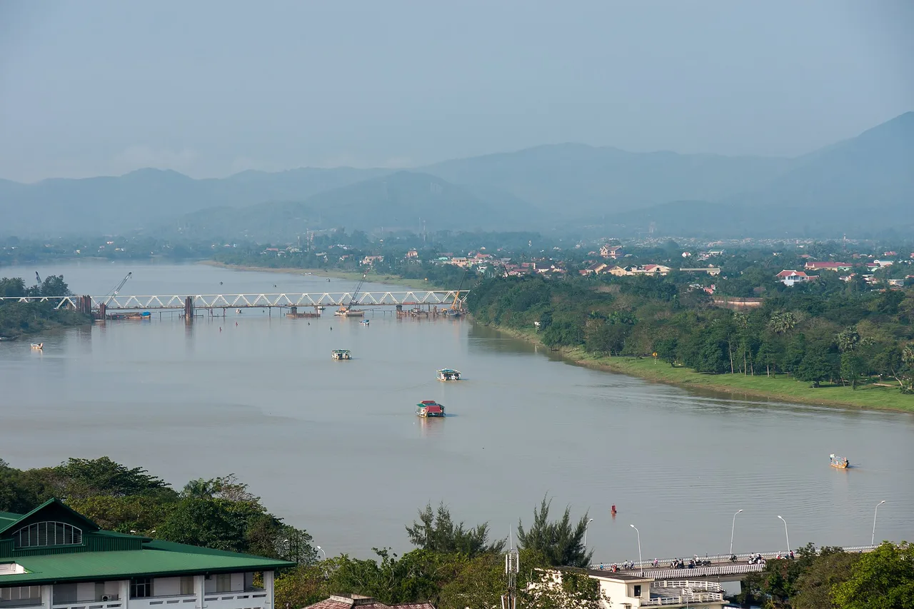 La large rivière des Parfums à Huế, un pont ferroviaire et des montagnes dans la brume